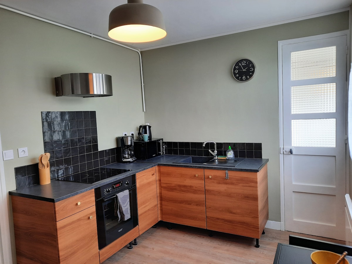 The kitchen features a combination of wooden cabinetry and black countertops, providing ample workspace. Essential appliances, including a coffee maker and oven, are arranged within easy reach. A clock is mounted on the wall, and a door to the outside is visible in the background.
