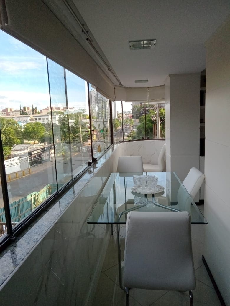 A bright dining area features a glass table surrounded by four white chairs. Large windows offer expansive views of the surrounding area, allowing natural light to fill the space. The sleek design emphasizes cleanliness and openness, with neutral tones throughout.