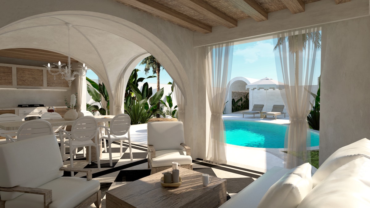 An airy living space features white furniture arranged around a wooden coffee table. Natural light floods the room through large arched openings with sheer curtains. Outside, a turquoise pool is framed by lush greenery and lounge chairs, creating a seamless indoor-outdoor connection.