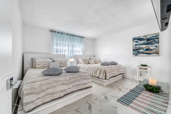 Chumba kikuu cha kulala chenye matandiko ya kifahari, mchoro wa majini na vipengele vya ubunifu wa pwani vya kutuliza