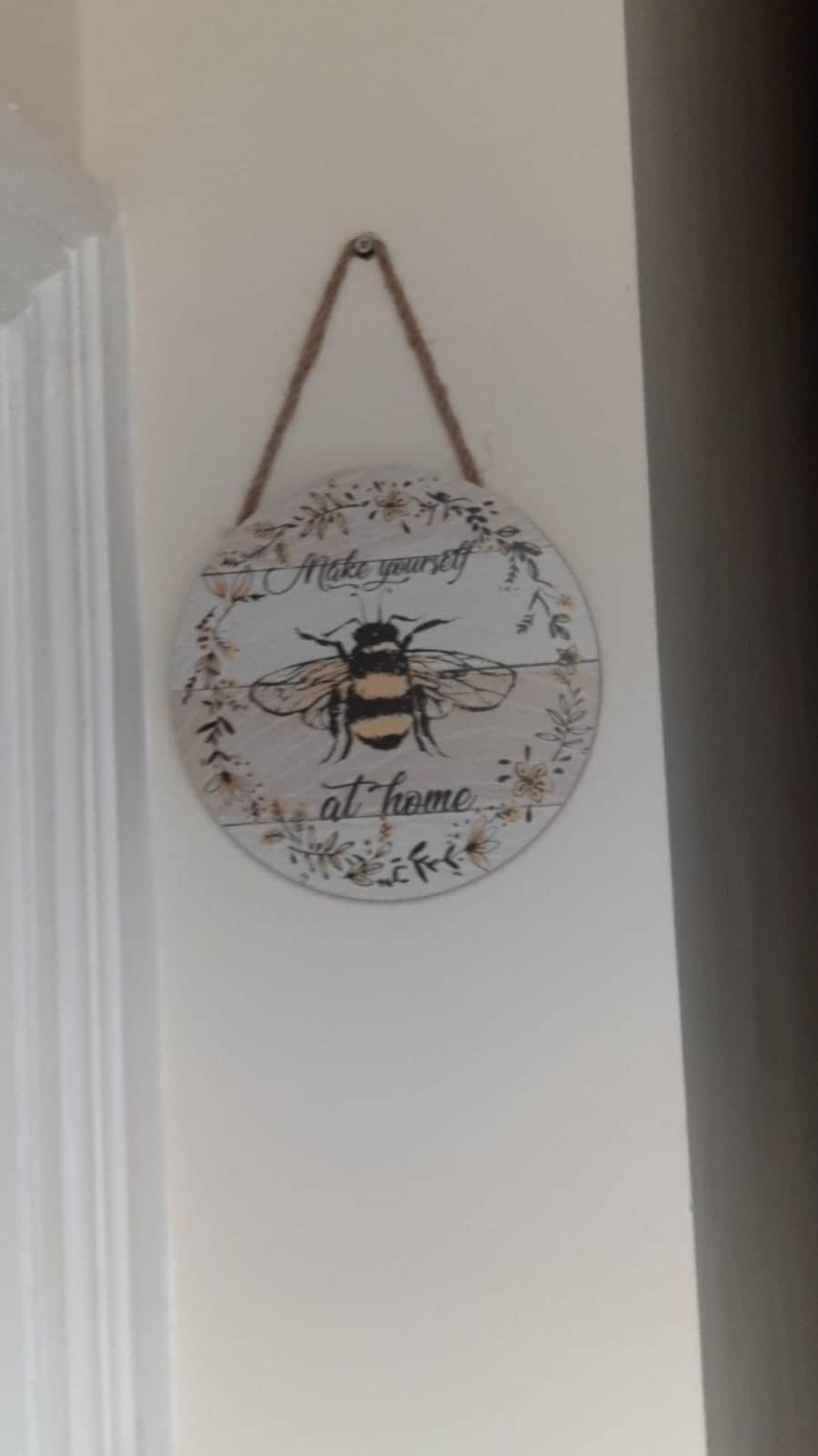 A decorative plaque is displayed on the wall, featuring a detailed illustration of a bee surrounded by floral elements. The words 'Make yourself at home' are artistically inscribed, inviting a warm sense of hospitality.