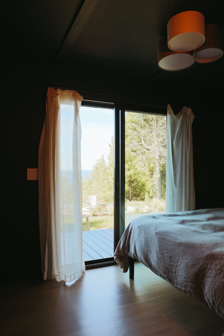 Dormitorio con una cama tamaño queen, puerta corrediza a la terraza y una vista increíble del lago