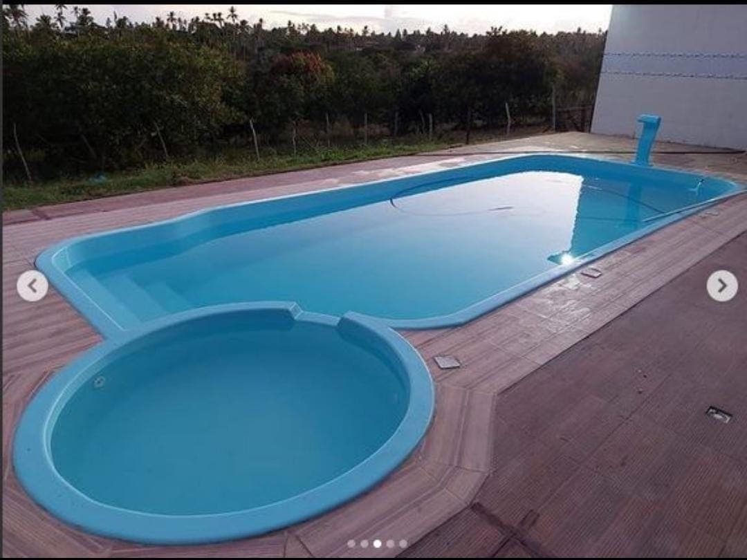 An inviting swimming pool is featured, designed in an elongated shape with a connected circular section. The clear blue water reflects the surrounding greenery, and a spacious deck area is visible, providing ample space for relaxation.