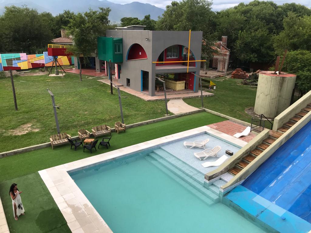 A spacious outdoor area features a vibrant, multi-colored building and a clear swimming pool bordered by lounge chairs. Lush greenery surrounds the space, with play equipment visible in the background, creating an inviting environment for relaxation and recreation.