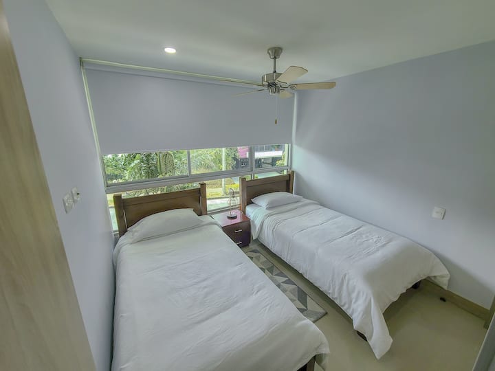 Спална соба бр. 2 со два единечни кревета и тавански вентилатор.