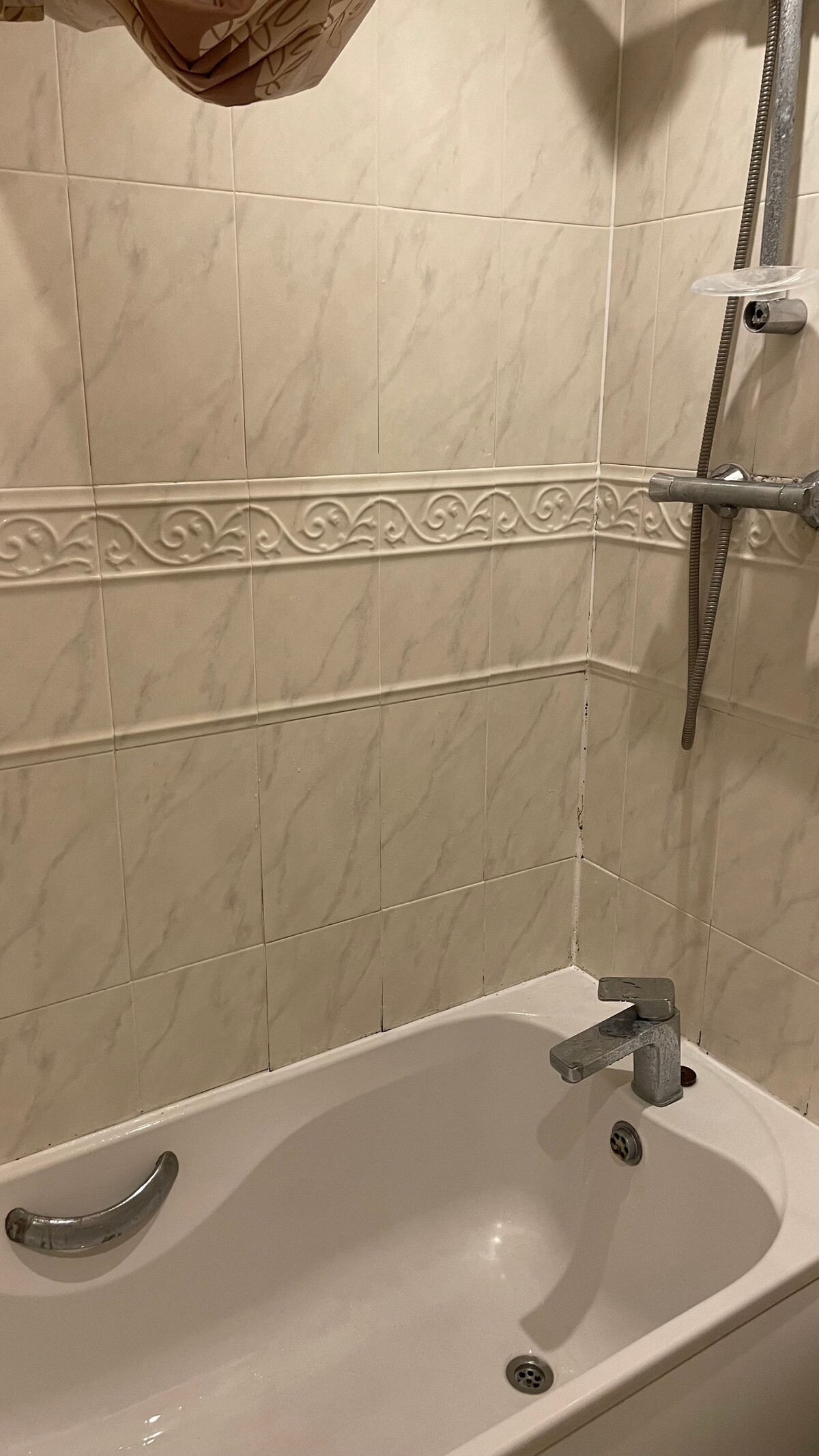 A clean and functional bathroom is presented, featuring a white bathtub with a sleek chrome faucet. The walls are adorned with light-colored tiles, showcasing a simple decorative border. A showerhead is mounted above, indicating a combined shower and bath setup.