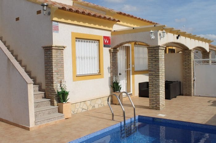 The exterior of the villa is shown, featuring a private swimming pool with steps for entry. A covered seating area is placed beside the pool, and a staircase leads up to the entrance of the house. The facade displays a mix of light-colored walls and brick detailing.