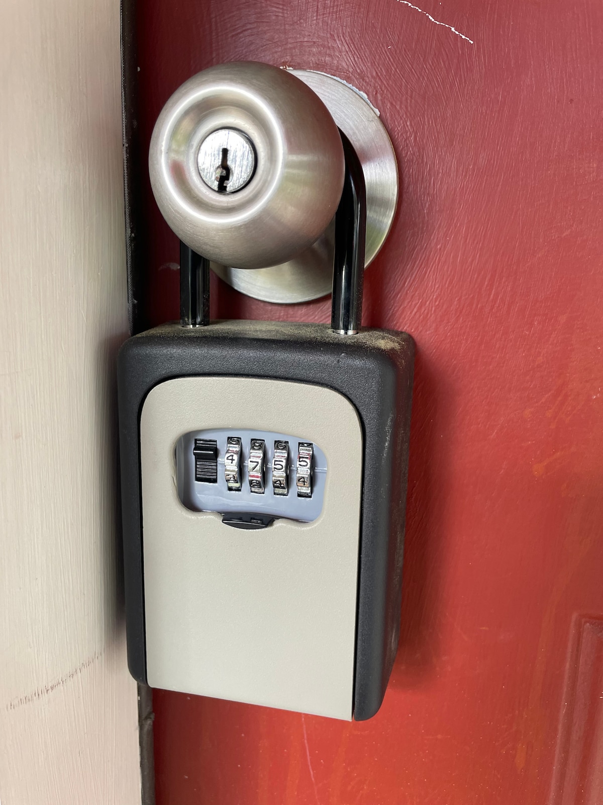 A secure combination lockbox is mounted next to a round door handle on a red door. The lockbox features a keypad with five visible dials, while a keyhole is positioned above it. The overall design emphasizes ease of access and security.