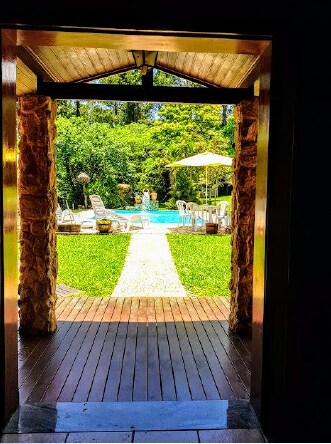 A view of the outdoor leisure area is framed by the entrance, revealing a tranquil pool surrounded by green grass. Patio furniture and an umbrella are visible near the water, offering a relaxed atmosphere for gatherings.