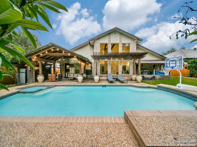 A private pool area is showcased with a clear blue water surface, surrounded by a landscaped yard. The spacious patio features comfortable lounge chairs and a shaded seating area under a pergola, creating a welcoming space for relaxation and gatherings.
