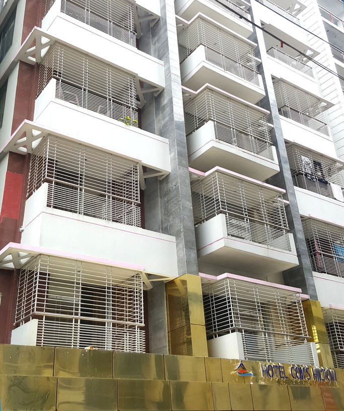 The exterior of the hotel showcases a modern design with multiple floors featuring light-colored balconies enclosed by metallic railings. A gold-accented entrance is displayed at the base, presenting the hotel name prominently against a sleek facade.