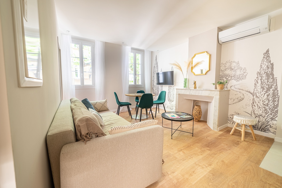 A bright living area features a comfortable sofa and a decorative fireplace. A dining table with chairs sits nearby. Large windows allow natural light to fill the space, while subtle decor elements enhance the modern atmosphere.