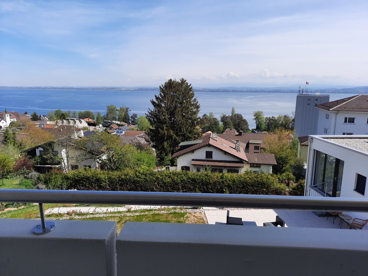 A panoramic view is captured from the balcony, showcasing a serene lake with distant mountains. The surrounding landscape features a mix of residential homes and lush greenery, enhancing the peaceful ambiance of the area.