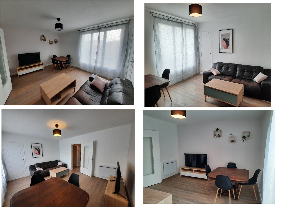 A shared living area is visible, featuring a television atop a light wood console. A dark sofa and a table accompanied by chairs occupy the space. Large windows allow natural light, with sheer curtains offering a soft, diffused glow throughout the room.
