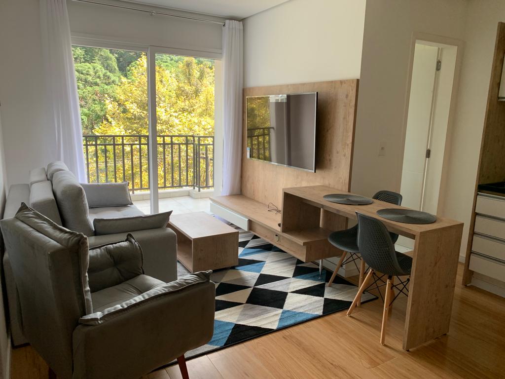 A modern living space features a comfortable gray sofa and an accent chair, complemented by a light wood media console with a flat-screen television. A dining table with stylish chairs is positioned on a geometric rug, with natural light filtering through large sliding glass doors, revealing views of greenery.