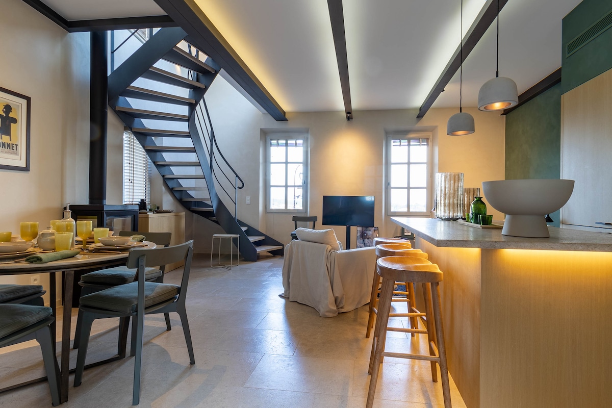 A spacious living area is highlighted by a modern open-plan kitchen and dining space. Natural light filters through large windows, illuminating the sleek design. A comfortable sofa is positioned near a wall-mounted television, while decorative elements enhance the inviting atmosphere.
