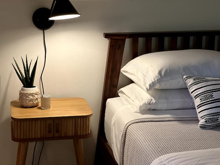 El dormitorio de arriba tiene una cama queen con colchón de espuma viscoelástica, sábanas de algodón suaves y mesas laterales con reloj despertador y lámparas de lectura regulables.