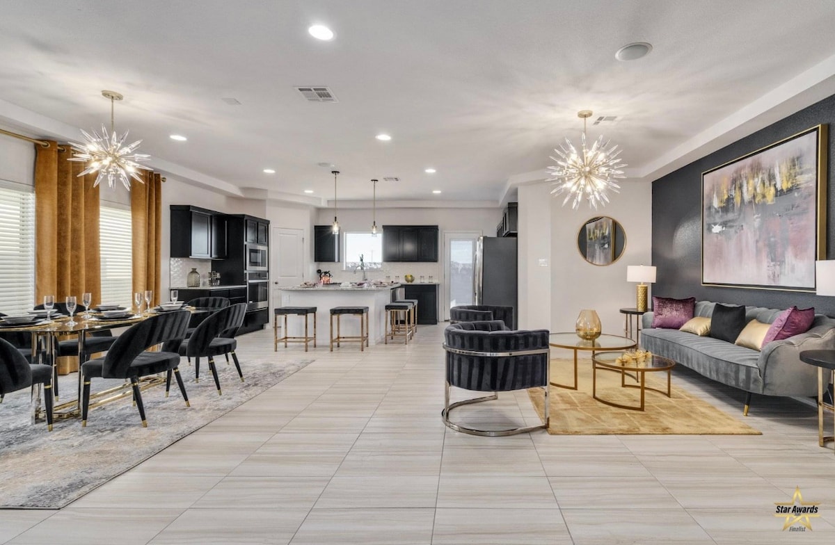 An open-concept living area is showcased, featuring a dining space with elegant table settings and modern light fixtures. The kitchen is visible in the background, equipped with sleek cabinetry and appliances. A cozy seating arrangement with plush chairs and a stylish sofa is positioned along a wall adorned with art.