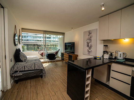 A modern studio apartment is showcased, featuring a seamless living and kitchen area. Large glass doors allow natural light to fill the space, revealing contemporary furnishings. A cozy bed is positioned beside a television, while a stylish dining area is complemented by sleek cabinetry.