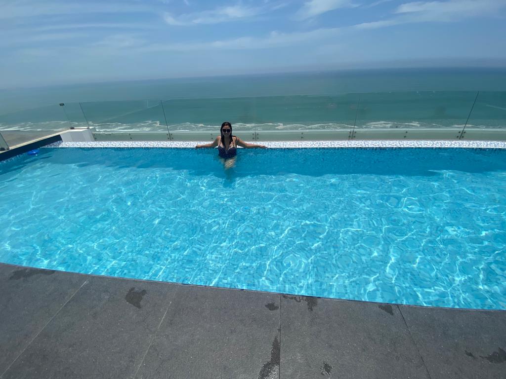 A panoramic pool located on the rooftop offers stunning ocean views. The clear, blue water reflects the sunlight, creating a tranquil ambiance. The surrounding glass railing enhances the view while ensuring safety. The horizon stretches out, showcasing the sea and sky meeting in the distance.