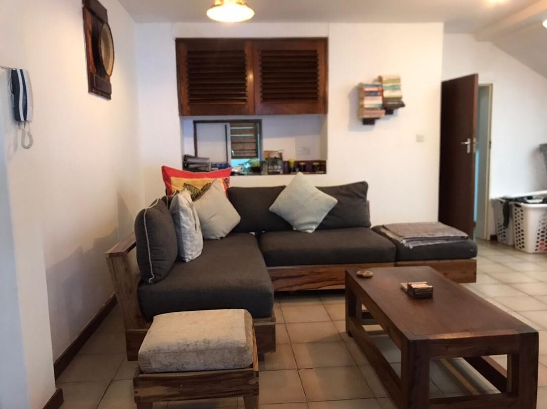 A modern living area is featured with a comfortable gray sectional sofa, complemented by plush cushions. A wooden coffee table sits in front, and a small ottoman adds seating options. Shelves are mounted on the wall, displaying a selection of books.