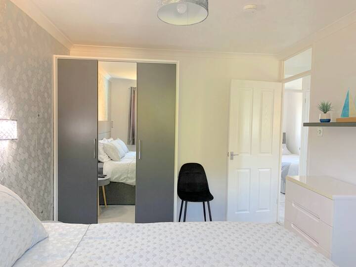 საძინებლის სუპერთასის ზომის საწოლი და 50-დუიმიანი კედელზე მიმაგრებული ტელევიზორი ცისა და სპორტული არხებით