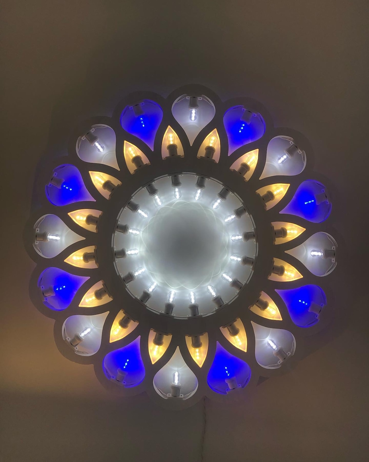 A decorative ceiling light fixture is featured, arranged in a floral pattern. The design incorporates a circular arrangement of blue, white, and warm yellow elements, creating a soft, inviting glow in the center. The fixture contributes a distinct visual appeal to the space.
