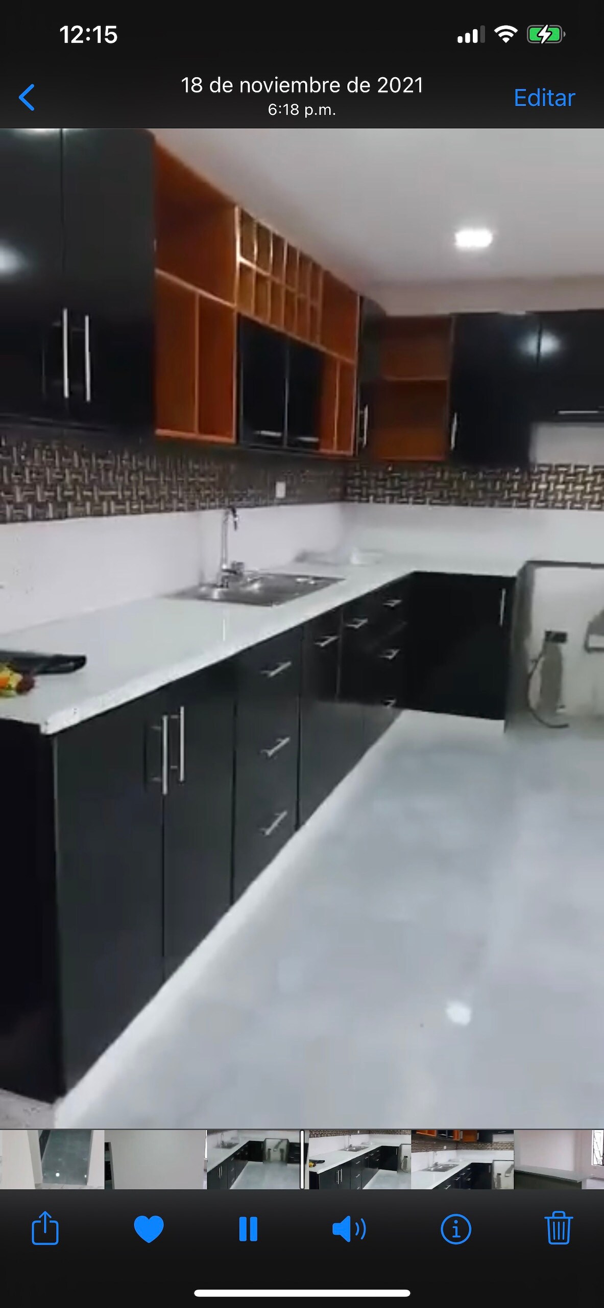 A modern kitchen is presented with sleek black cabinetry and white countertops. Open shelving is featured above the countertop, and a stainless steel sink is positioned for convenience. The floor is finished in a light tone, complementing the overall contemporary design.