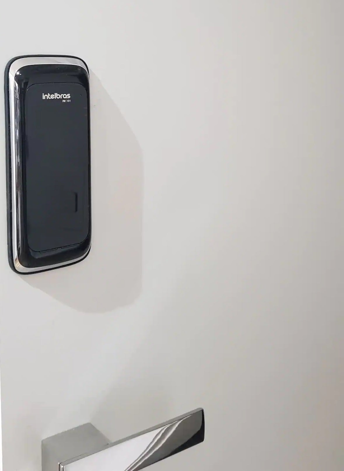 A modern door lock system is displayed on a sleek, white door. The lock features a glossy black panel with a silver trim, suggesting a contemporary security feature. A shiny chrome door handle complements the overall design.