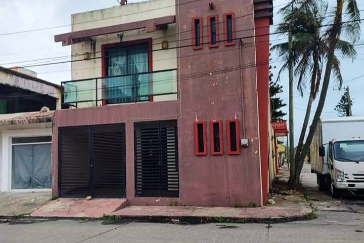 A two-story building is presented with a combination of textured materials and vibrant colors. Large windows allow natural light, and a balcony is visible on the second floor. The ground level features a modern facade with horizontal slatted elements and a recessed entrance.