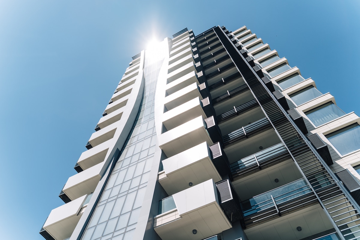 The Symphony Complex is featured prominently against a clear blue sky. Its modern architectural design includes a unique curving facade and multiple balconies, reflecting light from the sun. The building's sleek lines and glass elements create an impressive visual presence.