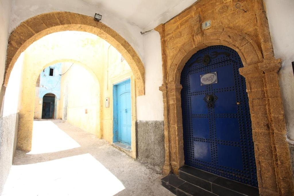 A sunlit alleyway is framed by two arches, showcasing textured stone walls. A vibrant blue door is positioned prominently, complemented by a lighter blue door in the background. The ground is composed of cobblestone, creating a charming and inviting atmosphere.