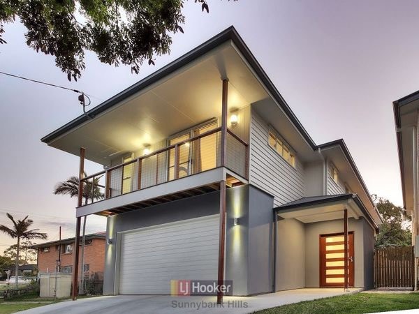 A modern two-story house is presented, featuring a sleek exterior with a prominent balcony. Outdoor lighting adds a warm glow to the entrance, which is complemented by landscaped greenery. A spacious garage is visible beneath the balcony, enhancing the home's functionality.