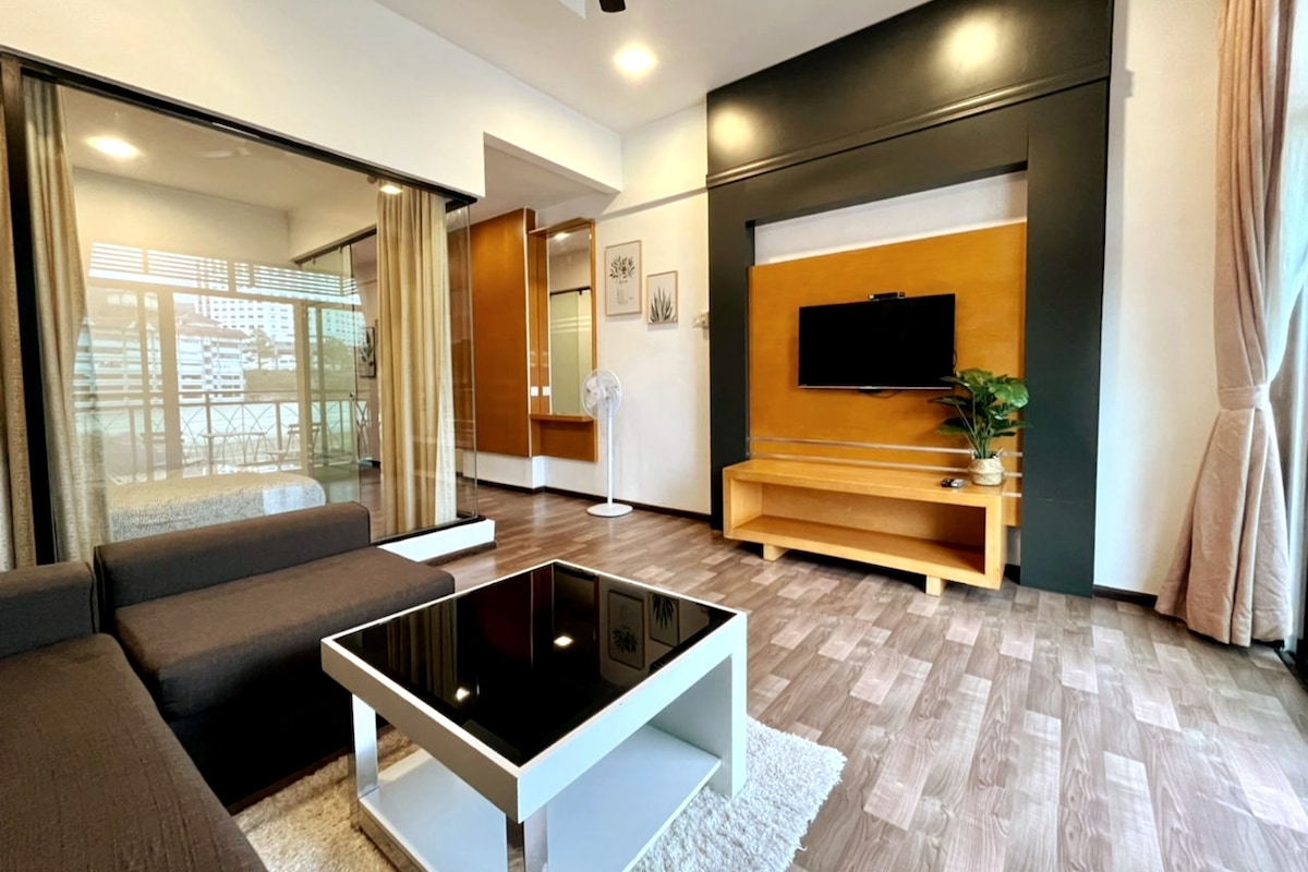 A modern living area is featured, showcasing a dark sectional sofa and a sleek coffee table with a glossy black top. A minimalist entertainment center houses a television, and large windows allow natural light to flow in, complemented by light curtains.