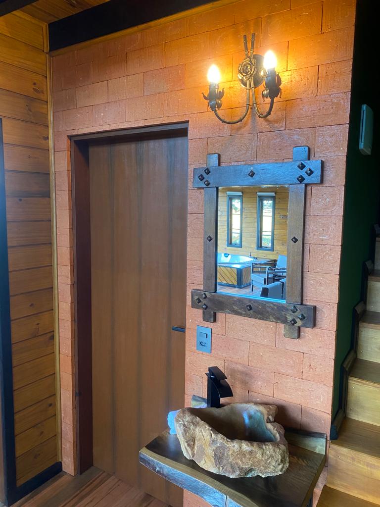 An entryway features a wooden door and a natural stone sink, accompanied by a decorative mirror framed in dark wood. Warm light is provided by an elegant wall sconce, enhancing the rustic charm of the space.