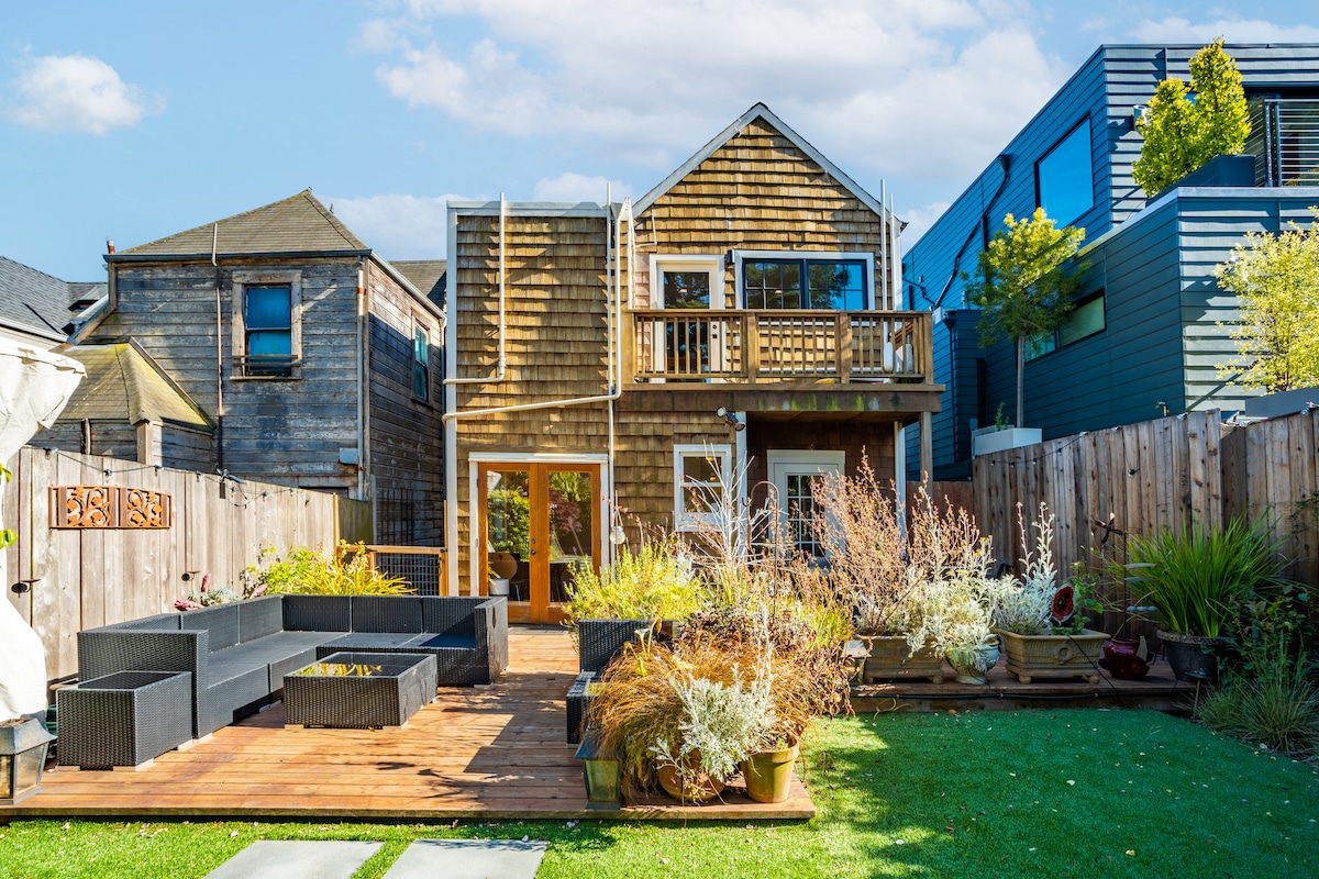 The beautifully landscaped yard features a spacious wooden deck with multiple seating areas surrounded by greenery. A manicured grass area complements the natural elements, while a second deck is visible in the background, enhancing the outdoor experience.