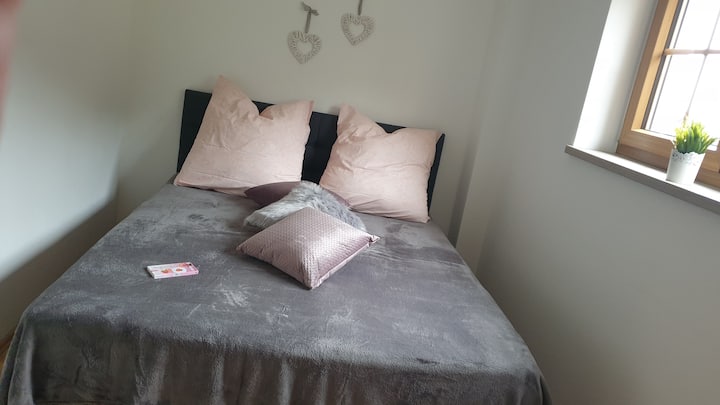 קומת קרקע בחדר השינה עם חלון בקומת הקרקע (על צלע גבעה) הפונה דרומה עם מזרן קופסאות בגודל 1,6x2 מ' וטלוויזיה חכמה בגודל 55אינץ '. Amazon Prime Video ו - Amazon Music ניתנים לשימוש בחינם. מתחת לטלוויזיה יש מדף עם 8 תאים וסלי בד כחלל אחסון