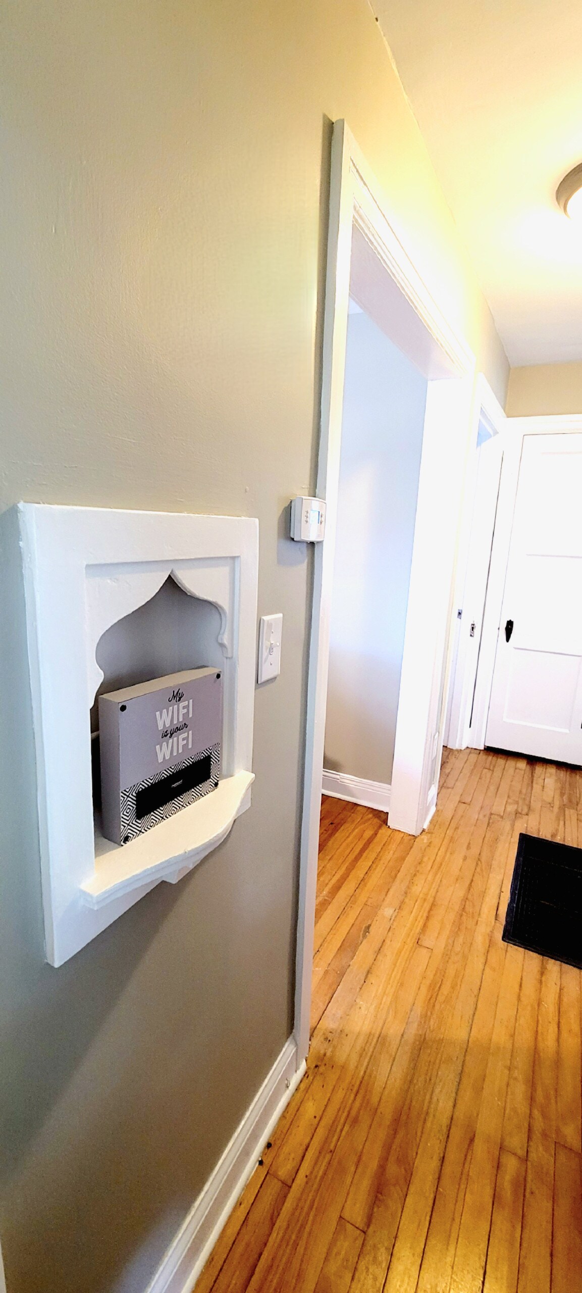 A hallway is displayed, revealing light hardwood flooring and smooth grey walls. A small wall-mounted sign indicates the presence of WiFi, positioned on the left side. Doorways lead to other rooms, contributing to an open and welcoming feel.