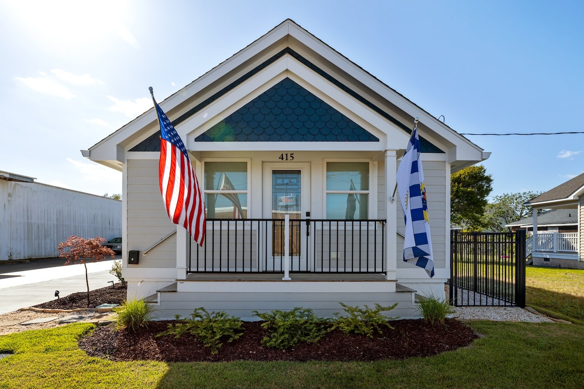 A charming exterior view showcases a single-story home with a gabled roof and vibrant blue accents. Two flags, an American flag and a decorative flag, flank the entrance. The well-maintained front yard features green landscaping and a small flowerbed, providing an inviting first impression.