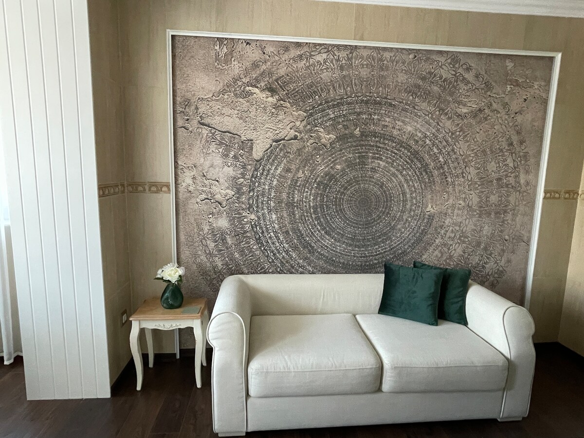 A light-colored sofa is positioned in front of an intricate world map mural that adds depth to the space. A small table beside the sofa is adorned with a vase of fresh flowers, enhancing the room's comfort and elegance.