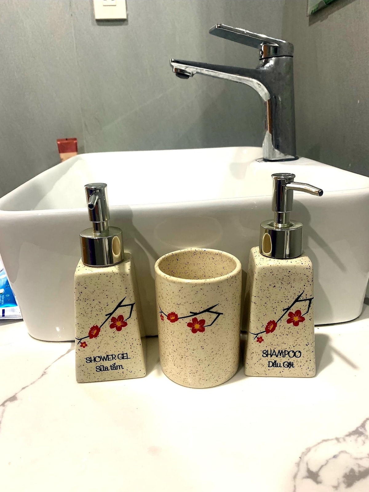 A modern sink area features a square white basin with a sleek faucet. Two decorative containers for shower gel and shampoo are positioned next to a cup, all designed with a floral pattern, enhancing the functional and aesthetic elements of the space.