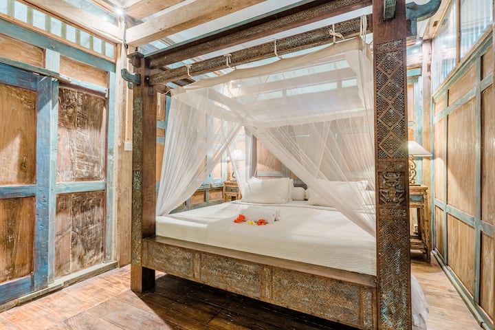 Një dhomë gjumi romantike me një krevat të madh, mobilie druri dhe ndriçim të butë. Dhoma ka një atmosferë të rehatshme dhe intime, e përkryer për një gjumë të qetë gjatë natës.