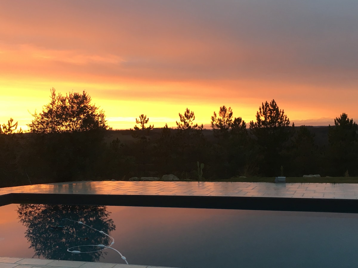 A tranquil pool reflects the soft hues of a sunset, with the sky transitioning from orange to a darker shade. Surrounding trees illustrate the natural landscape, providing a serene backdrop to the tranquil setting.