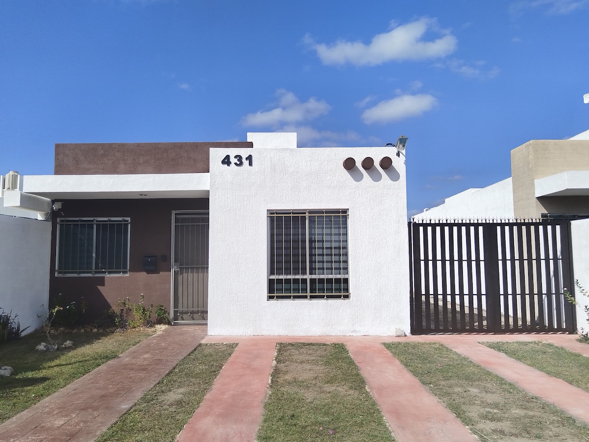 The exterior of the house features a white facade with brown accents, marked by the number 431. A gated entrance provides security, while a neatly landscaped yard is framed by grass and a fully paved pathway leading to the entrance.