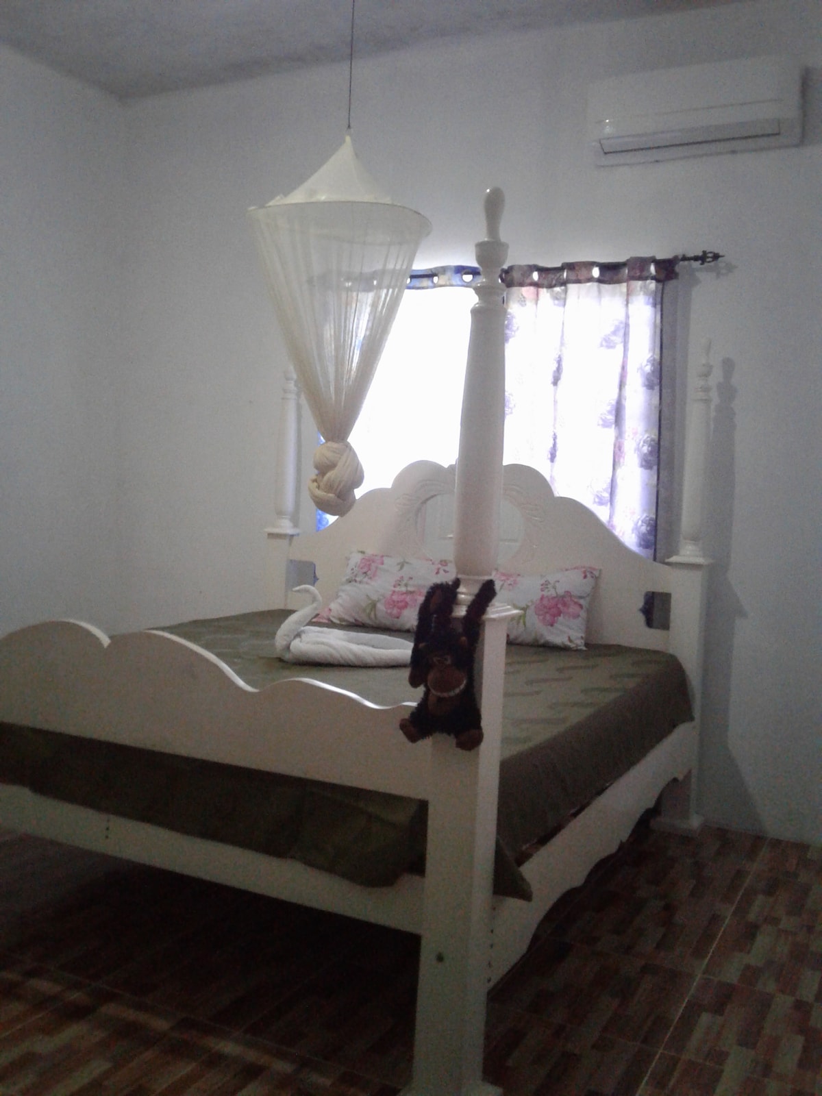 A tranquil sleeping area features a spacious bed with a decorative headboard and a green bedspread. A mobile hangs from the ceiling above the bed, while floral curtains frame the window, allowing natural light to filter into the room.