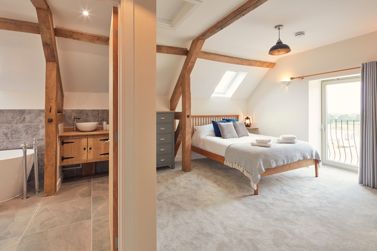 Amplio dormitorio en suite con una cama tamaño king y un balcón de Julieta con vistas a las colinas de los Cotswolds