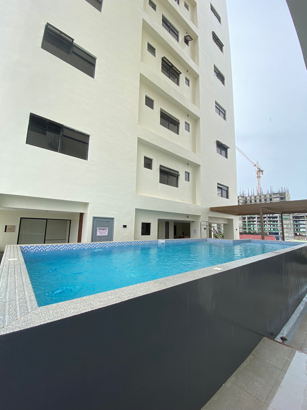 A serene swimming pool is showcased adjacent to the building, with clear blue water reflecting the surrounding structure. The clean lines of the modern architecture are visible, alongside large windows that invite natural light into the indoor areas of the residence.