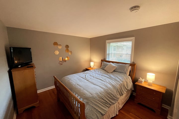 เตียงควีนไซส์ขนาดใหญ่พร้อมโครงเตียงไม้จริงและตู้เสื้อผ้า/โต๊ะข้างเตียงที่เข้าชุดกันสมาร์ททีวี Roku รวมอยู่ในห้องนอน 