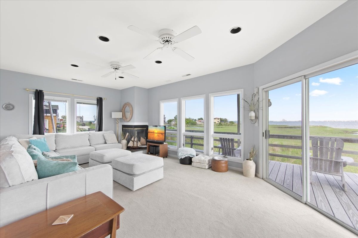 The living room features a spacious sectional sofa, positioned to face a large window offering scenic views of the outdoors. A cozy fireplace adds warmth, while light-colored walls and soft carpet create a calm environment. Sliding doors provide access to the deck.