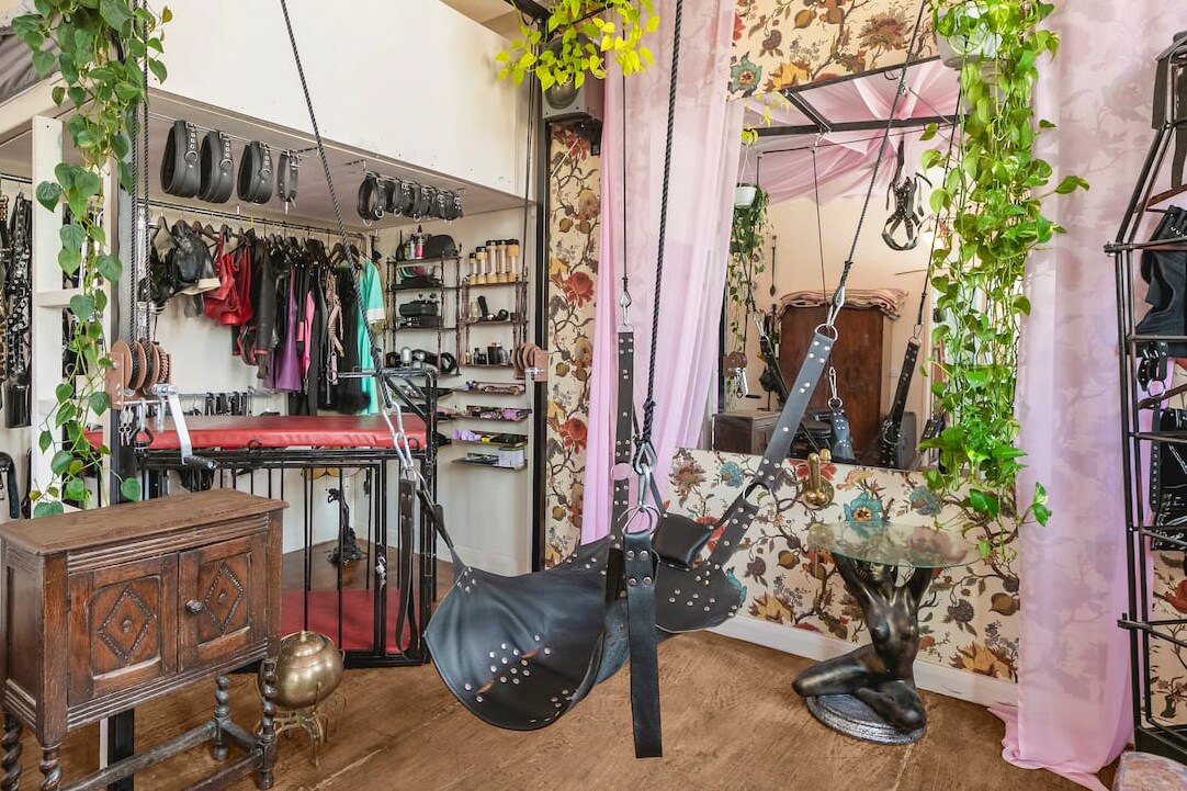 A multifunctional space is highlighted by a leather swinging seat, positioned in front of a large mirror. Shelves display an array of equipment against a backdrop of floral wallpaper and greenery, adding a layer of texture and interest to the room.